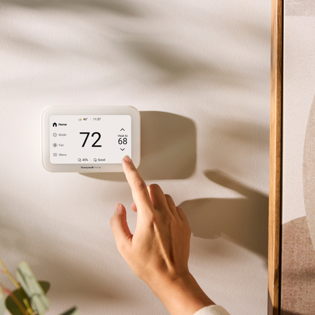 Hand adjusting a Honeywell Home smart thermostat displaying 72°F on a wall.