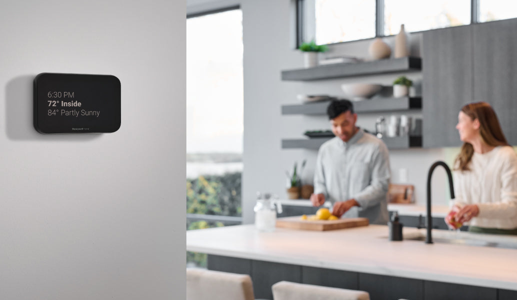 X8S smart thermostat displaying weather information in a kitchen setting with two people.