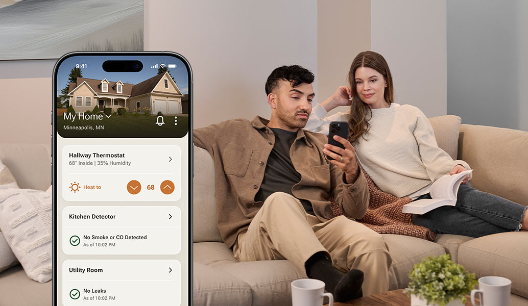 A man and woman sit on a couch while using the Resideo Connect app.