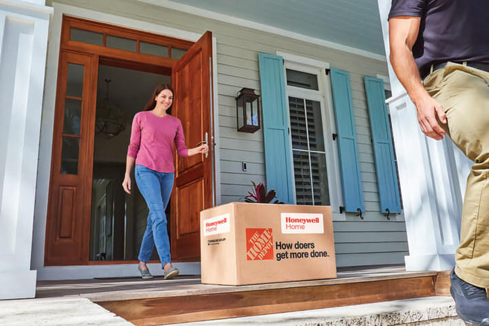 Woman receiving a package from a delivery person at her front door with The Home Depot box.