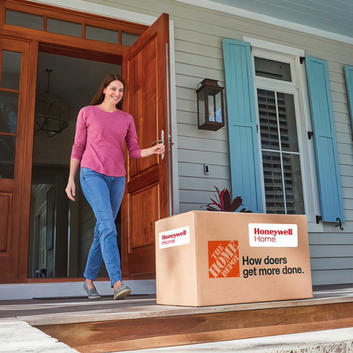 A woman receives a package on her porch. The package has the Home Depot logo and the Honeywell Home logo along with text that reads: How doers get more done.