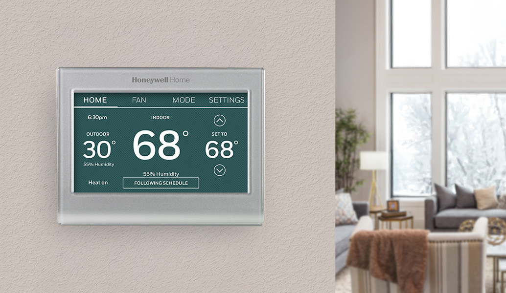 Green colored thermostat installed on wall with living room in background